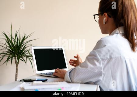 Rear view female business person sitting at the desk and having online video meeting using her laptop. Stock Photo