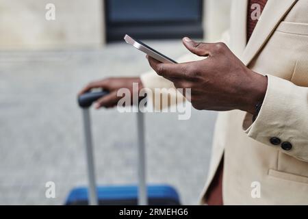 Close-up of young businessman in white formalwear texting in smartphone while standing in front of camera outdoors and waiting for taxi Stock Photo