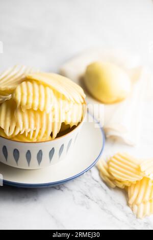 Slices and whole potatoes placed on a white marble board. Stock Photo