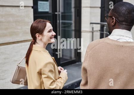 Young smiling businesswoman in beige formalwear looking at African American male colleague while discussing working points with him Stock Photo