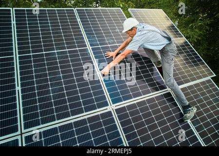 Male worker in safety helmet installing photovoltaic solar panels. Man in work overalls assembling solar modules for generating electricity through the photovoltaic effect. Stock Photo