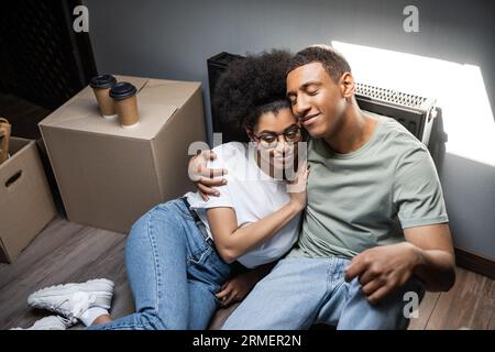high angle view of smiling african american couple hugging near coffee on attic in new house Stock Photo
