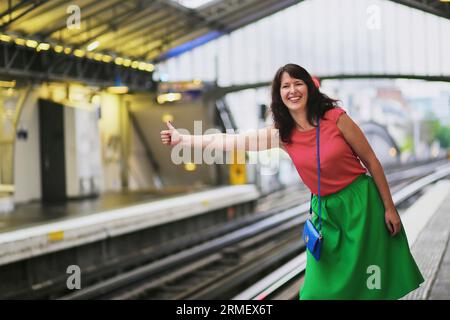 Cheerful young woman in Paris having fun in Parisian underground and pretending to hitch-hike a train Stock Photo