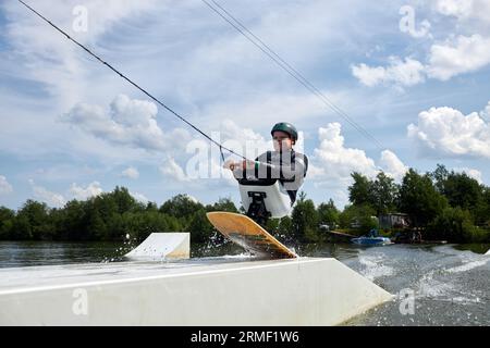 Action portrait of young man with disability enjoying fast speed wakeboarding jumping off ramp with adaptive equipment, copy space Stock Photo