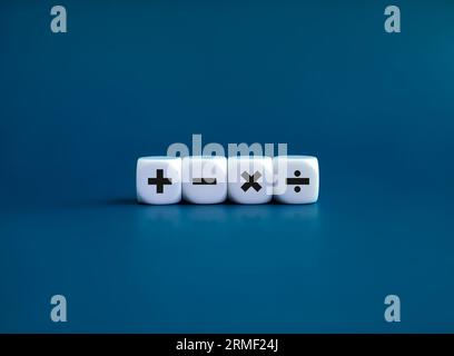 Plus, minus, multiplication and division signs on white dice cube blocks isolated on blue background, minimal style. Financial, mathematics and calcul Stock Photo
