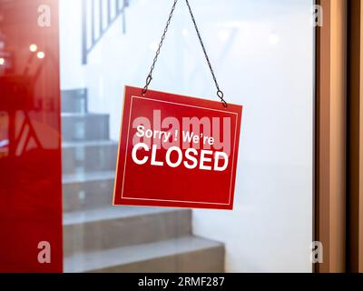 Shop closed, red and white notice sign with words 'Sorry ! we're closed' hanging on glass door in front of the staircase in the hotel or restaurant. N Stock Photo