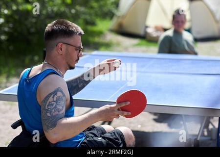 Side view portrait of young man with disabilty playing table tennis with partner outdoors Stock Photo