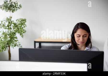 Smiling mid adult businesswoman using headset in office in front of computer screen Stock Photo