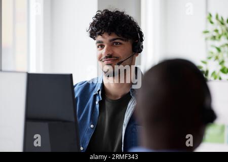 Young man using headset while sitting in office Stock Photo