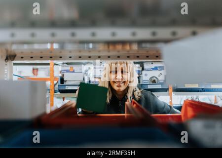 Portrait of smiling female worker taking equipment from shelf Stock Photo