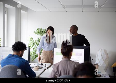Man and woman talking inn office while other coworkers using computers Stock Photo