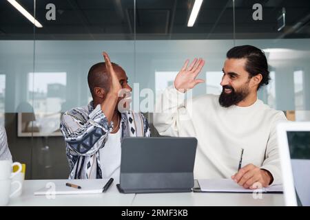 Smiling coworkers sitting at business meeting and giving each other high five Stock Photo