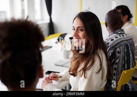Smiling woman sitting during business meeting and looking at colleague Stock Photo