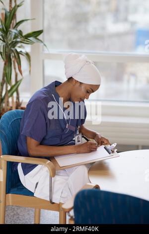 Female doctor looking sitting at table and taking notes Stock Photo