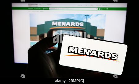 Person holding smartphone with logo of US retail company Menard Inc. (Menards) on screen in front of website. Focus on phone display. Stock Photo