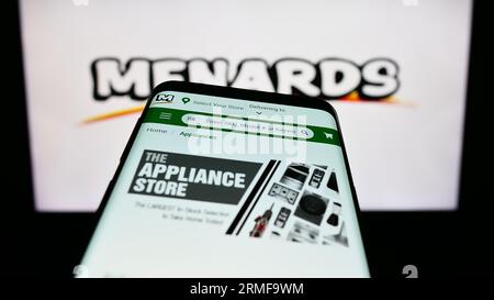 Mobile phone with webpage of US retail company Menard Inc. (Menards) on screen in front of business logo. Focus on top-left of phone display. Stock Photo