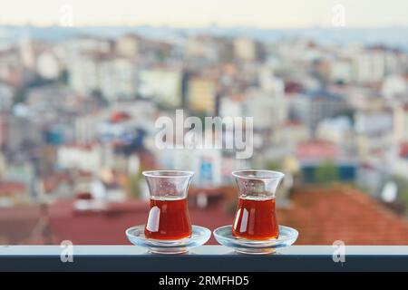 Two Turkish glasses in form of a tulip filled with hot black tea with view to the roofs of Uskudar district on Asian side of Istanbul, Turkey Stock Photo