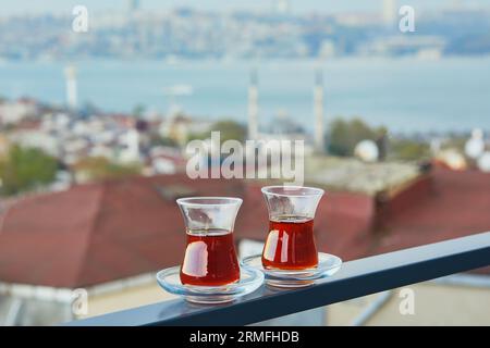 Two Turkish glasses in form of a tulip filled with hot black tea with view to the roofs of Uskudar district on Asian side of Istanbul, Turkey Stock Photo