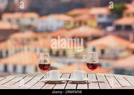 Two glasses of Madeira wine and two cups of fresh espresso coffee in street cafe with view to Funchal town, Madeira, Portugal Stock Photo