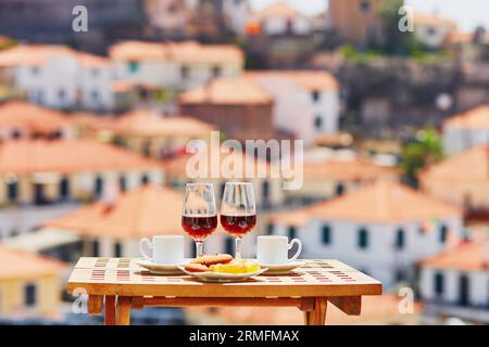 Two glasses of Madeira wine and two cups of fresh espresso coffee in street cafe with view to Funchal town, Madeira, Portugal Stock Photo