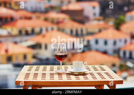 Glasse of Madeira wine and cup of fresh espresso coffee in street cafe with view to Funchal town, Madeira, Portugal Stock Photo