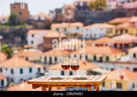 Two glasses of Madeira wine and two cups of fresh espresso coffee in cafe with view to Funchal town, Madeira, Portugal Stock Photo