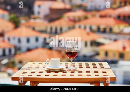 Glasse of Madeira wine and cup of fresh espresso coffee in street cafe with view to Funchal town, Madeira, Portugal Stock Photo