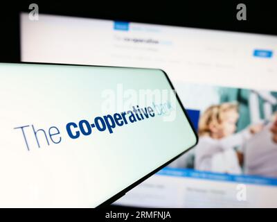 Smartphone with logo of British company The Co-operative Bank plc on screen in front of website. Focus on center-left of phone display. Stock Photo