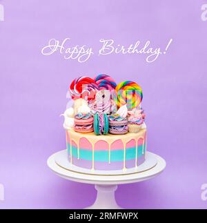 Cololrful and bright birthday cake with lollipops and sweets over a purple background with copy space Stock Photo