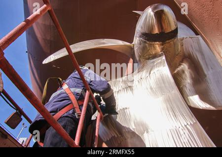 man repairing a ship propeller using a handheld saw .propeller ship maintenance. dry dock. Stock Photo