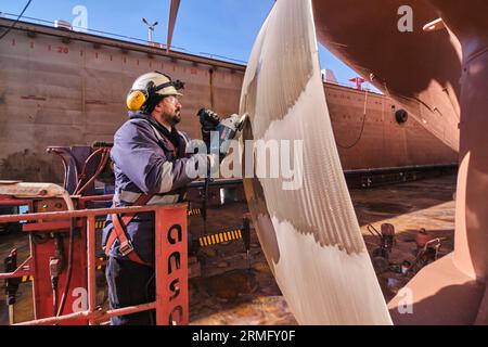 man repairing a ship propeller using a handheld saw .propeller ship maintenance. dry dock. Stock Photo