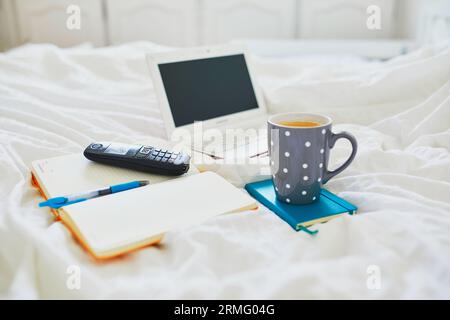 Laptop, notebook and phone in bed on clean white linens. Freelance, distance learning or work from home concept Stock Photo