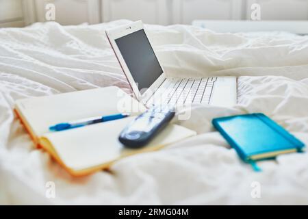 Laptop, notebook and phone in bed on clean white linens. Freelance, distance learning or work from home concept Stock Photo