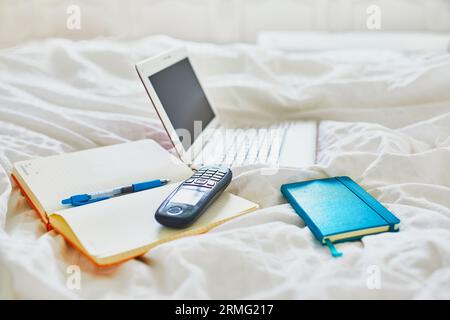 Laptop, notebook and phone in bed on clean white linens. Freelance, distance learning or work from home concept Stock Photo
