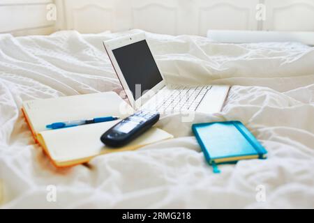 Laptop, notebook and phone in bed on clean white linens. Freelance, distance learning or work from home concept Stock Photo