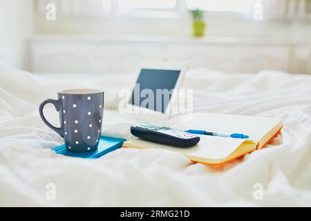 Laptop, cup of coffee, notebook and phone in bed on clean white linens. Freelance, distance learning or work from home concept Stock Photo