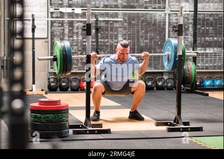 Full body of determined male athlete in sportswear doing back squats with heavy barbell during intense workout in gym Stock Photo