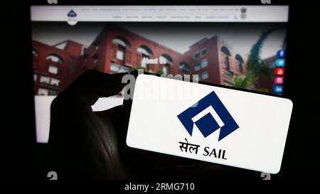 Person holding cellphone with logo of company Steel Authority of India Limited (SAIL) on screen in front of webpage. Focus on phone display. Stock Photo