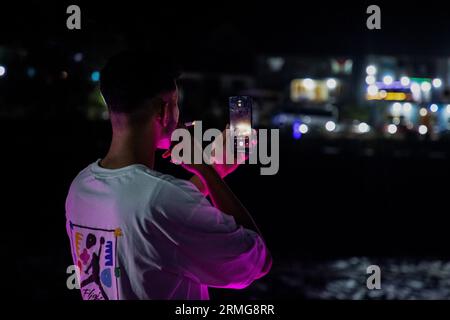 August 24, 2023, Keran Kupwara, Jammu and Kashmir, India: A local visitor seen smoking while filming towards Pakistan administered Kashmir during evening on the banks of Neelam river or Kishan Ganga that has divided Kashmir into two parts controlled by nuclear rivals India and Pakistan. The river acts as a disputed line of control and flows through a village called Keran from both sides which is located on the northern side of Indian Kashmir's Border district Kupwara some 150kms from Srinagar and 93kms from Muzaffarabad, in the Pakistan side of Kashmir. (Credit Image: © Faisal Bashir/SOPA Imag Stock Photo