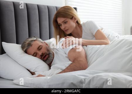 Irritated woman waking up her snoring husband in bed at home Stock Photo