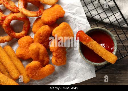 Tasty chicken nuggets, fried onion rings, cheese sticks and ketchup on wooden table, top view Stock Photo