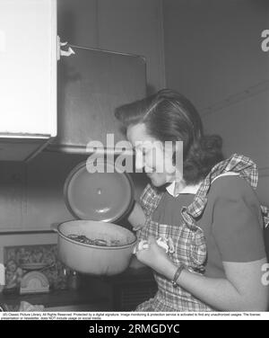 In the kitchen 1940s. Interior of a kitchen and a young woman lifting the lid of a saucepan steaming hot and looks happy with how it turned out. Sweden 1946 Kristoffersson ref CC122-1 Stock Photo