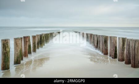 Wave breakers on the beach of Domburg in the Netherlands. Long exposure photo with dynamic waves breaking at the shore on wooden poles Stock Photo