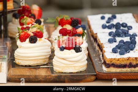 Confectionery stall at the Prague farmers market with desserts on display, close-up of blueberry pie and pavlova embellished with fresh fruit, strawbe Stock Photo