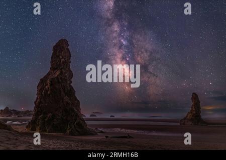 The Milky Way stretches out of the Pacific Ocean between two sea stacks on Bandon Beach, Oregon. Stock Photo