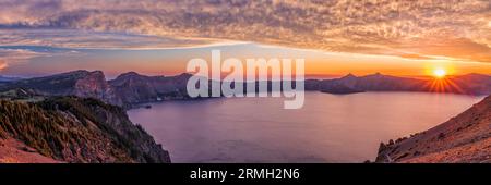 The setting sun over the West Rim of Crater Lake in a panoramic view captured on Cloudcap viewpoint in Crater Lake National Park, Oregon. Stock Photo