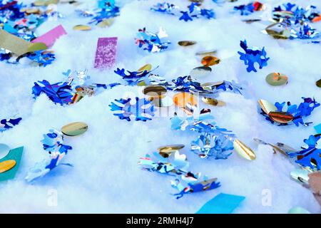 Ornate confetti and ribbons from a cracker is scattered on fresh snow. Holidays and events backgrounds Stock Photo