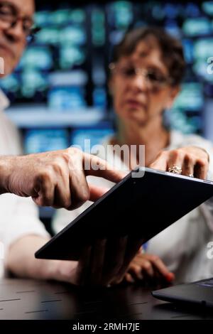 Elderly engineers working to maintain uptime in high tech data center. Experienced technicians brainstorming solutions to server hub infrastructure crashing, trying to repair equipment, close up Stock Photo