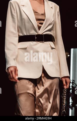 Fashionable details of classy white jacket, silk skirt and leather belt on a female figure. Designer collection clothes. Catwalk Fashion Week Stock Photo