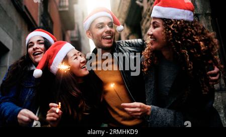 Happy diverse friends celebrate Christmas party with sparkler fireworks outdoors - Multi-ethnic group of people having fun during December holidays Stock Photo